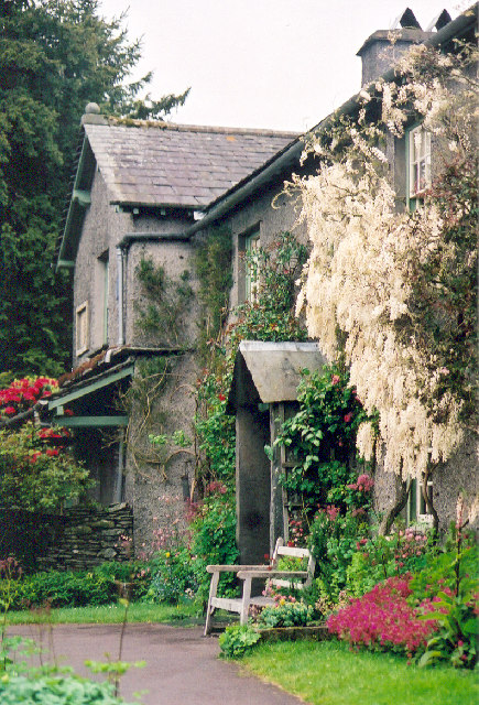 An image of a grey house, Hill Top Farm in Cumbria, with flowers growing around it and a bench out front.