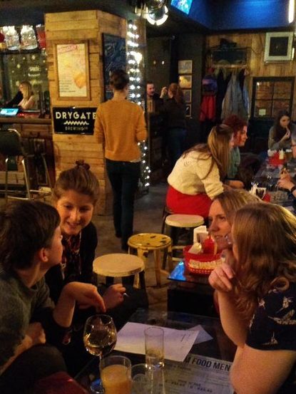 4 people in the foreground are huddled around a table in a bar