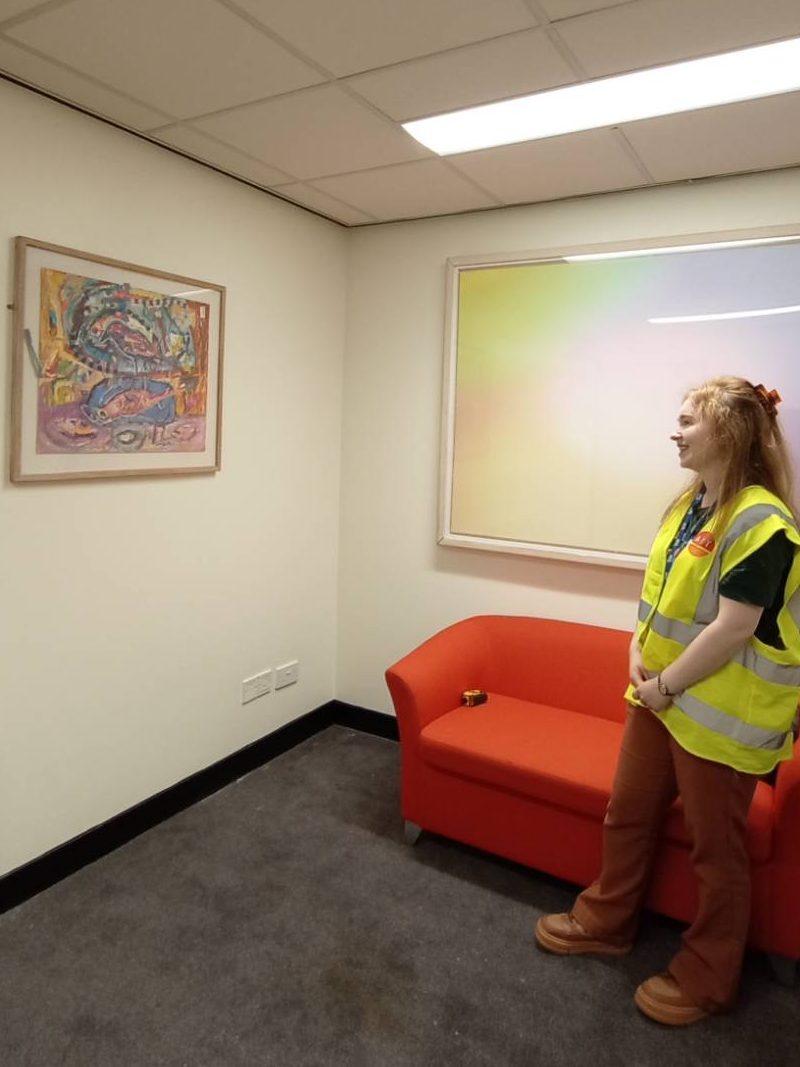 A person stands off to the right hand side, looking at a colourful painting on the wall